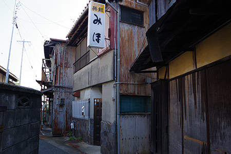 豊川（駅前通り南側の路地）飲食店の斜めドア。 古今東西舎